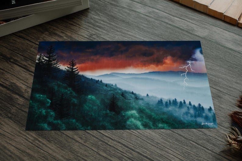 以下が含まれることがあります： 劇的な空の下の山脈を描いた風景画。このアートワークは、霧のかかった森林の丘の上に稲妻が走る鮮やかな夕焼けを特徴としています。カラーパレットには、緑、青、オレンジの色合いが含まれています。