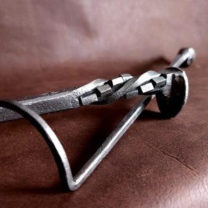 Op de afbeelding: Een metalen haardgereedschap met een gedraaide handgreep en een haak aan het ene uiteinde. Het gereedschap is gemaakt van ijzer en heeft een rustieke afwerking.