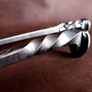 Op de afbeelding: Twee metalen haardgereedschappen met gedraaide handvatten. De gereedschappen zijn gemaakt van staal en hebben een rustieke afwerking.