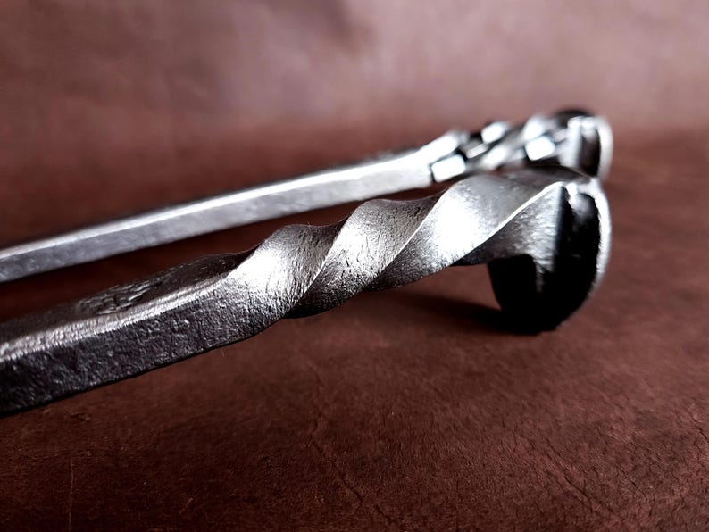 Op de afbeelding: Twee metalen haardgereedschappen met gedraaide handvatten. De gereedschappen zijn gemaakt van staal en hebben een rustieke afwerking.