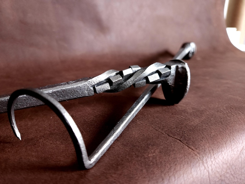 Op de afbeelding: Een metalen haardgereedschap met een gedraaide handgreep en een haak aan het ene uiteinde. Het gereedschap is gemaakt van ijzer en heeft een rustieke afwerking.