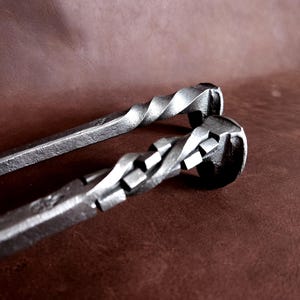 Op de afbeelding: Twee metalen haardgereedschappen met gedraaide handvatten. De gereedschappen zijn gemaakt van staal en hebben een rustieke afwerking.