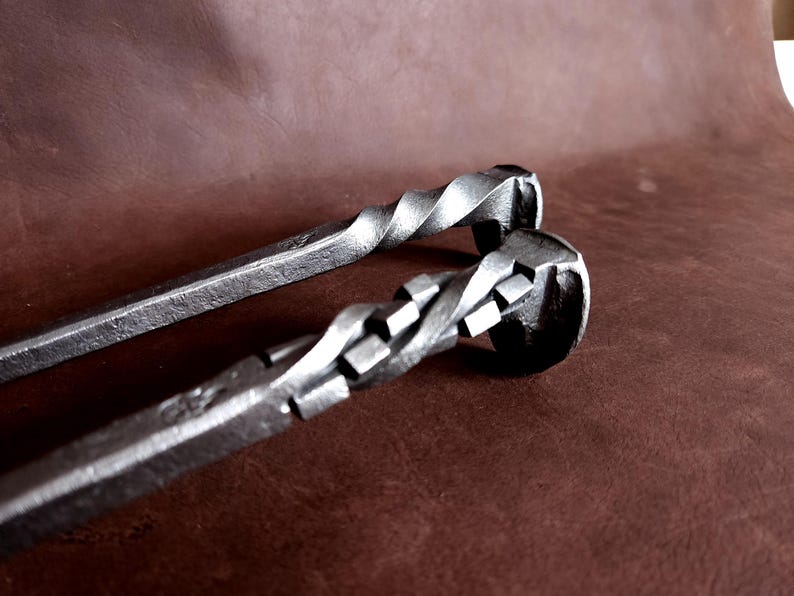 Op de afbeelding: Twee metalen haardgereedschappen met gedraaide handvatten. De gereedschappen zijn gemaakt van staal en hebben een rustieke afwerking.