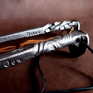 May include: Two metal bottle openers with leather straps. One opener has a braided design and the name "BRIAN" engraved on it. The other opener has a wavy design and the name "JON" engraved on it.