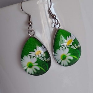 May include: A pair of silver teardrop earrings with a green background and white daisy flowers.