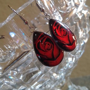 May include: A pair of silver dangle earrings with red rose cameo pendants. The rose is a dark red with black shading.