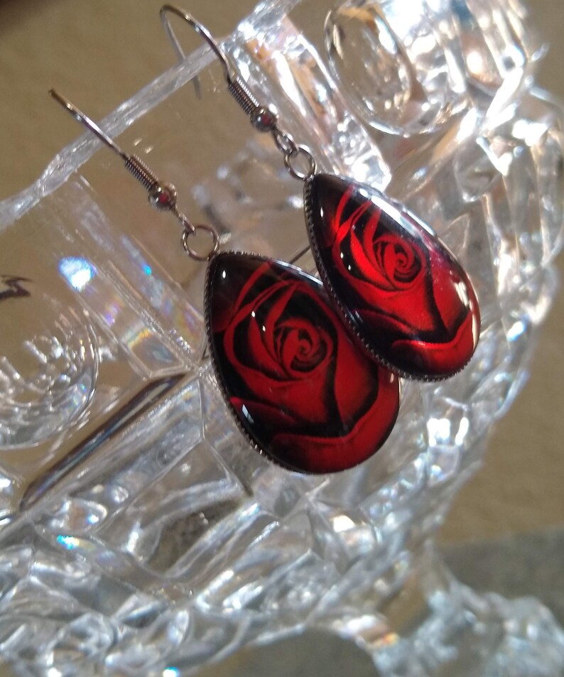 May include: A pair of silver dangle earrings with red rose cameo pendants. The rose is a dark red with black shading.