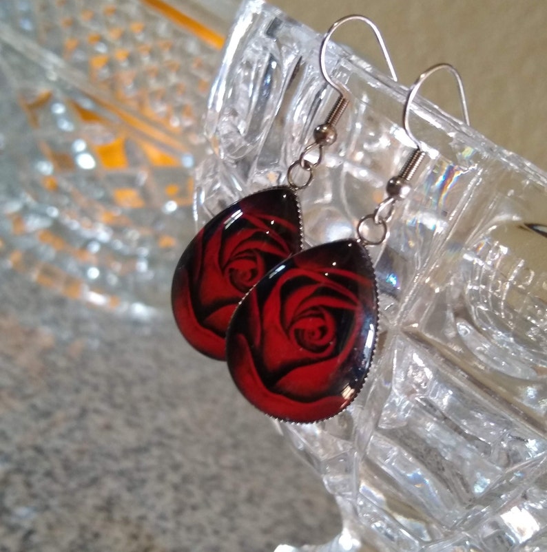 May include: A pair of dangle earrings with a teardrop-shaped red rose design.