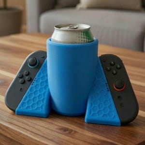 Pode incluir: Um suporte de bebida de silicone azul com dois controladores de jogo pretos e azuis. O suporte contém uma lata prateada. Os controladores têm um padrão de favo de mel. Os itens estão em uma mesa de madeira.