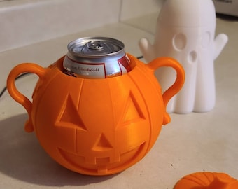 Puede incluir: Portabebidas naranja en forma de calabaza con una cara de calabaza y dos asas. Una lata plateada está dentro del portabebidas. Un portabebidas blanco en forma de fantasma está en el fondo.