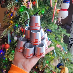 May include: A stack of silver-colored metal containers with red numbers "10" on each container. The containers are arranged in a pyramid shape on a hand.