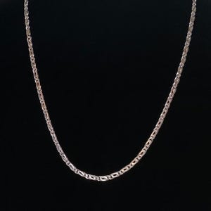 May include: A silver-colored chain necklace with a repeating oval and rectangular link design. The necklace is displayed against a black background, highlighting its reflective surface and intricate pattern. The chain is delicate and appears to be made of metal.