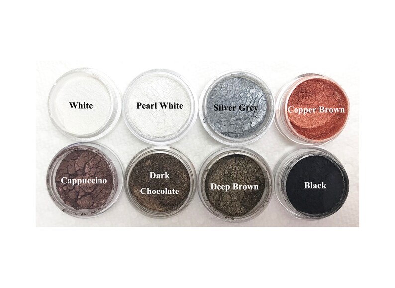Puede incluir: Ocho peque&ntilde;os recipientes circulares transparentes llenos de pigmentos cosm&eacute;ticos en polvo de colores. Las etiquetas dicen White, Pearl White, Silver Grey, Copper Brown, Cappuccino, Dark Chocolate, Deep Brown y Black, dispuestos en dos filas.