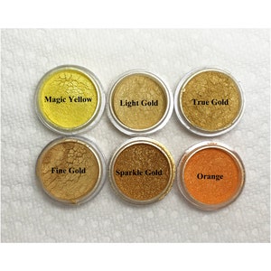 Puede incluir: Seis recipientes circulares de pigmento en polvo dispuestos en dos filas. Los colores est&aacute;n etiquetados como Magic Yellow, Light Gold, True Gold, Fine Gold, Sparkle Gold y Orange. Cada recipiente presenta un acabado met&aacute;lico o vibrante.