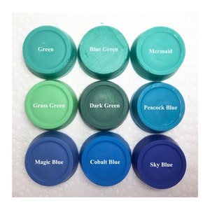 Puede incluir: Nueve recipientes circulares de cera o pigmento de colores dispuestos en una cuadr&iacute;cula de tres por tres. Las etiquetas dicen Green, Blue Green, Mermaid, Grass Green, Dark Green, Peacock Blue, Magic Blue, Cobalt Blue y Sky Blue en blanco.
