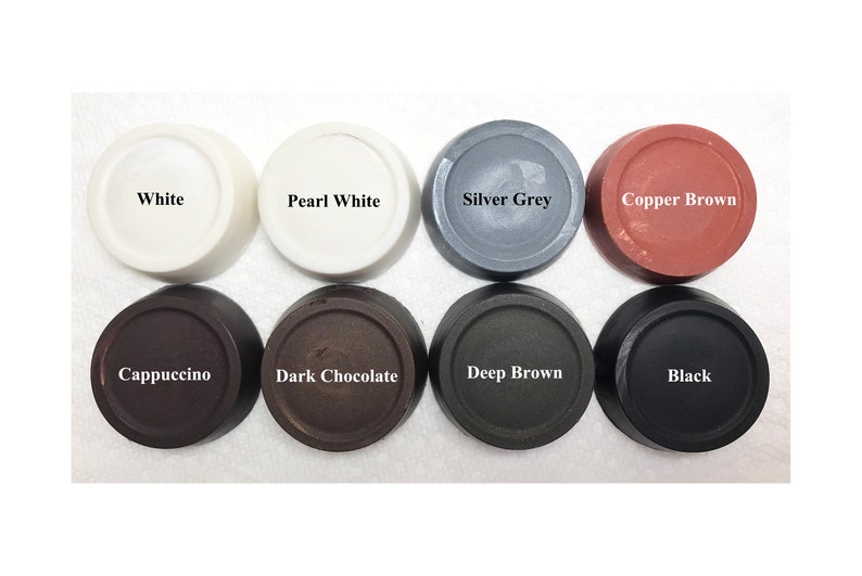 Puede incluir: Ocho botones circulares dispuestos en dos filas, etiquetados con los nombres de los colores: White, Pearl White, Silver Grey, Copper Brown, Cappuccino, Dark Chocolate, Deep Brown y Black. Cada bot&oacute;n tiene un acabado liso y plano.