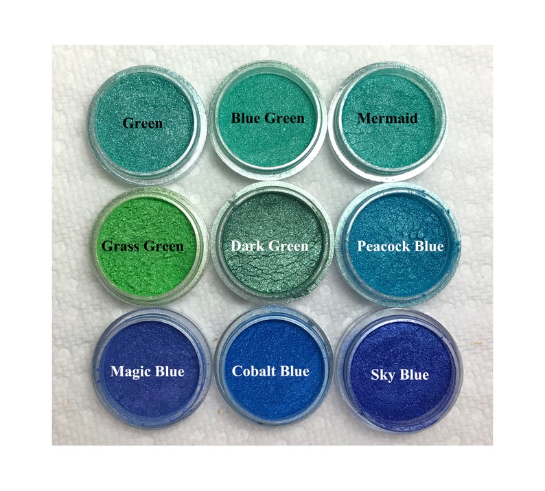 Puede incluir: Nueve recipientes circulares llenos de polvo de mica brillante en varios tonos de verde y azul. Las etiquetas dicen Green, Blue Green, Mermaid, Grass Green, Dark Green, Peacock Blue, Magic Blue, Cobalt Blue y Sky Blue.
