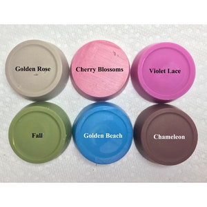 May include: Six round containers of different colors with text labels: Golden Rose, Cherry Blossoms, Violet Lace, Fall, Golden Beach, Chameleon.