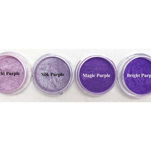 Puede incluir: Cuatro recipientes circulares transparentes llenos de polvo de mica morado en varios tonos. Las etiquetas dicen Light Purple, Silk Purple, Magic Purple y Bright Purple. Cada recipiente contiene un pigmento fino y brillante con acabado met&aacute;lico.