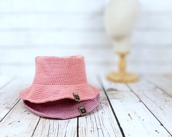 May include: Two pink crocheted bucket hats stacked on top of each other. The hats have a simple design and are made with a soft, textured yarn.