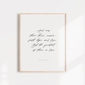 Puede incluir: Una impresión enmarcada con fondo blanco y texto en caligrafía negra. El texto dice "Y ahora permanecen estas tres cosas: la fe, la esperanza y el amor. Pero la más grande de estas es el amor." El texto es de 1 Corintios 13:13.
