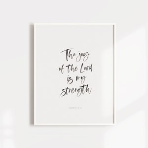 Puede incluir: Una impresión enmarcada en blanco con caligrafía negra que dice "La alegría del Señor es mi fortaleza" con la referencia bíblica "Nehemías 8:10" debajo.