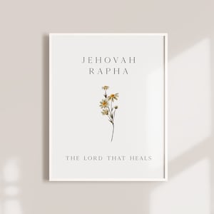 Puede incluir: Impresión enmarcada con las palabras "JEHOVAH RAPHA" y "THE LORD THAT HEALS" en texto negro. Una pequeña ramita floral con flores blancas y amarillas está centrada debajo del texto. El marco es blanco.