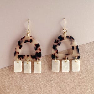 Peut inclure: Une paire de boucles d'oreilles en ton or avec une arche à motif de carapace de tortue et trois pendentifs rectangulaires blancs.