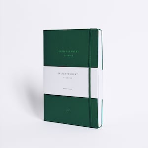 May include: A dark green planner with a white band that says "Enlightenment Planner" and "Gratitude everyday". The planner has a green elastic band and a green lotus flower logo.