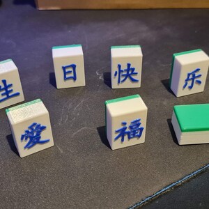 May include: Seven white tiles with green and blue accents. Each tile has a Chinese character written in blue on the top surface. The characters are: 生, 愛, 日, 快, 符, 福, and a blank tile with a green top.