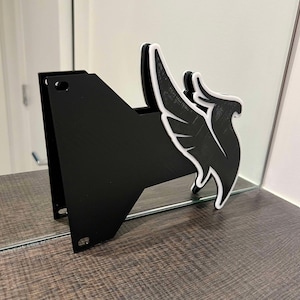 May include: A black wall mount with a white stylized bird design. The mount is made of plastic and has a smooth surface.