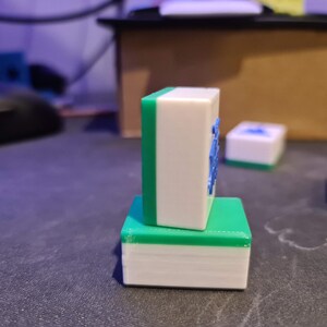 May include: Two green and white mahjong tiles stacked on top of each other. The top tile has blue characters on it.