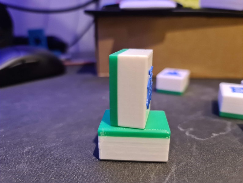 May include: Two green and white mahjong tiles stacked on top of each other. The top tile has blue characters on it.