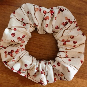 May include: A white fabric scrunchie with a brown and red floral pattern. The pattern features small red berries and brown branches.