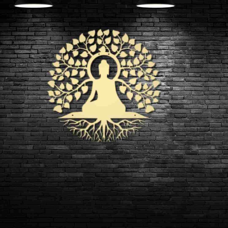 Puede incluir: Una pieza de arte mural de metal dorado que representa una figura de Buda sentado bajo un &aacute;rbol con hojas. La obra de arte est&aacute; montada en una pared de ladrillo gris oscuro, creando un contraste entre el oro claro y el fondo oscuro. El dise&ntilde;o es intrincado y detallado.