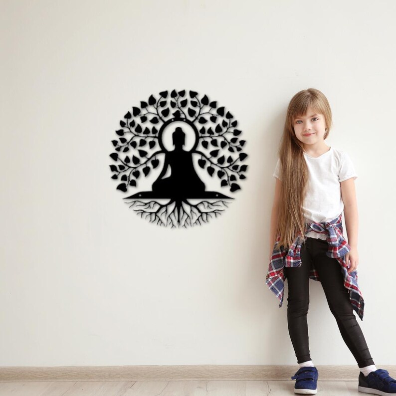 Puede incluir: Arte mural de metal negro que representa a un Buda sentado dentro de un &aacute;rbol. El dise&ntilde;o presenta una disposici&oacute;n circular de hojas, ra&iacute;ces y un halo alrededor del Buda. La obra de arte est&aacute; montada en una pared blanca.