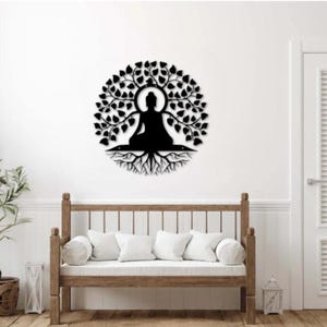 Puede incluir: Arte mural de metal negro que representa a un Buda meditando bajo un &aacute;rbol con hojas. La obra de arte circular presenta la silueta del Buda en el centro, con ra&iacute;ces visibles debajo. Montado en una pared blanca, ideal para la meditaci&oacute;n.