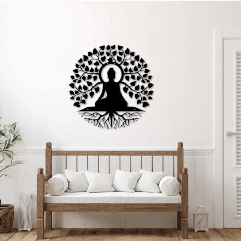 Puede incluir: Arte mural de metal negro que representa a un Buda meditando bajo un &aacute;rbol con hojas. La obra de arte circular presenta la silueta del Buda en el centro, con ra&iacute;ces visibles debajo. Montado en una pared blanca, ideal para la meditaci&oacute;n.