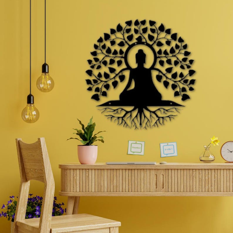 Puede incluir: Arte de pared de metal negro que representa a un Buda meditando bajo un &aacute;rbol. La imagen tambi&eacute;n muestra un escritorio de madera, una silla e iluminaci&oacute;n decorativa, todo sobre una pared amarilla.