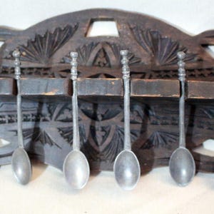 Peut inclure: Un porte-cuillères en bois sculpté avec des détails complexes, contenant six cuillères à café en argent. Le porte-cuillères est en forme de croissant de lune et a une finition brun foncé.