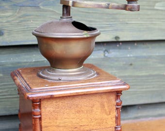 Op de afbeelding: Oude koffiemolen van hout en messing. De molen heeft een houten basis met een kleine lade, een messing trechter en een houten slinger. De hendel is bekroond met een houten bal. Een vintage keukenartikel.