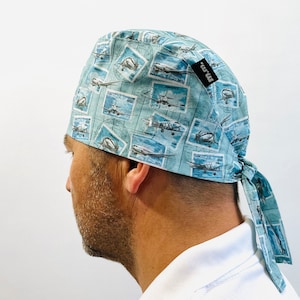 Puede incluir: Un gorro de quirófano azul y blanco con estampado y una corbata. El gorro presenta un patrón repetido de aviones en sellos postales. El gorro tiene una etiqueta negra con el texto "MRW" en el lateral.