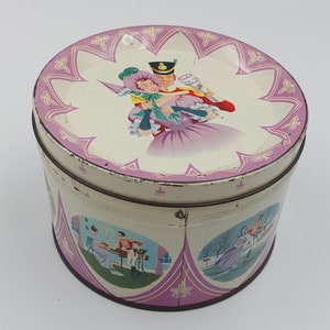Può includere: Una scatola vintage rotonda in latta con un design floreale rosa e bianco. Il coperchio presenta una coppia in abiti del XVIII secolo, mentre i lati raffigurano scene di persone in varie attività.