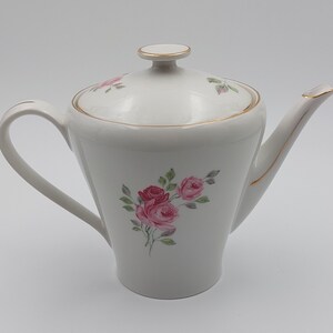 Peut inclure: Théière en porcelaine blanche avec une bordure dorée et un motif floral composé de roses roses et de feuilles vertes.