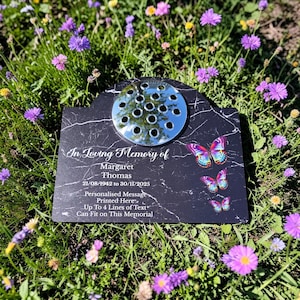 May include: A black marble memorial plaque with a silver flower holder and butterfly accents. The plaque reads "In Loving Memory of Margaret Thomas 21/08/1942 to 30/11/2025". It also states "Personalised Message Printed Here" and "Up To 4 Lines of Text".