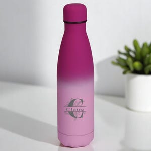 Könnte beinhalten: Eine rosafarbene und violette Ombre-Edelstahl-Wasserflasche mit einem personalisierten Design. Das Design zeigt ein florales Motiv und den Namen "Claire" mit einem Buchstaben "C" als Initial.