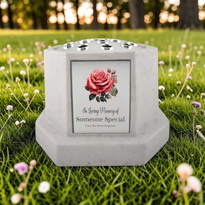 May include: A gray memorial vase with a floral design and the text "In Loving Memory of Someone Special". The vase has a top with multiple holes for flower stems and is set on a grassy lawn.