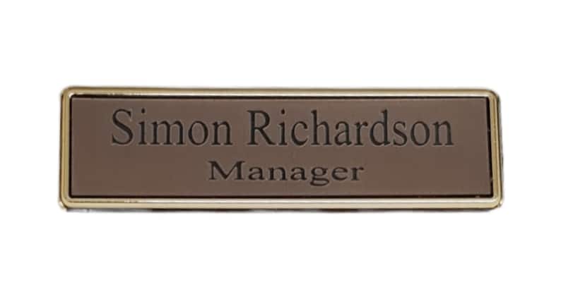 May include: A gold-framed name tag with a brown background. The name tag reads "Simon Richardson, Manager."