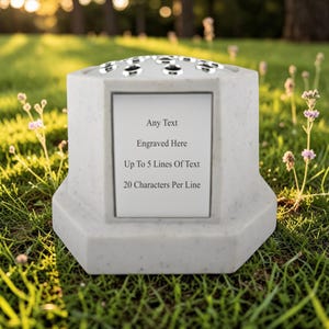 Peut inclure: Un vase commémoratif gris clair avec une base hexagonale et un dessus avec plusieurs ouvertures. Le vase a une zone rectangulaire pour la gravure, avec le texte "Any Text, Engraved Here, Up To 5 Lines Of Text, 20 Characters Per Line."