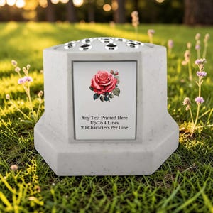 May include: A light gray memorial vase with a floral rose design. The vase has a rectangular inset with a red rose illustration and text that reads "Any Text Printed Here Up To 4 Lines 20 Characters Per Line". The top has multiple holes.